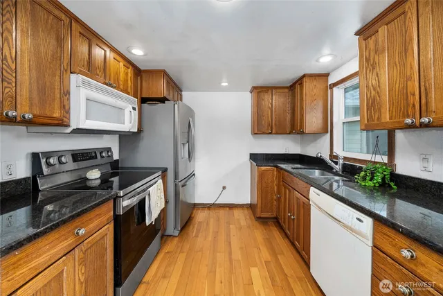 a kitchen with granite countertop wooden floors stainless steel appliances and a window