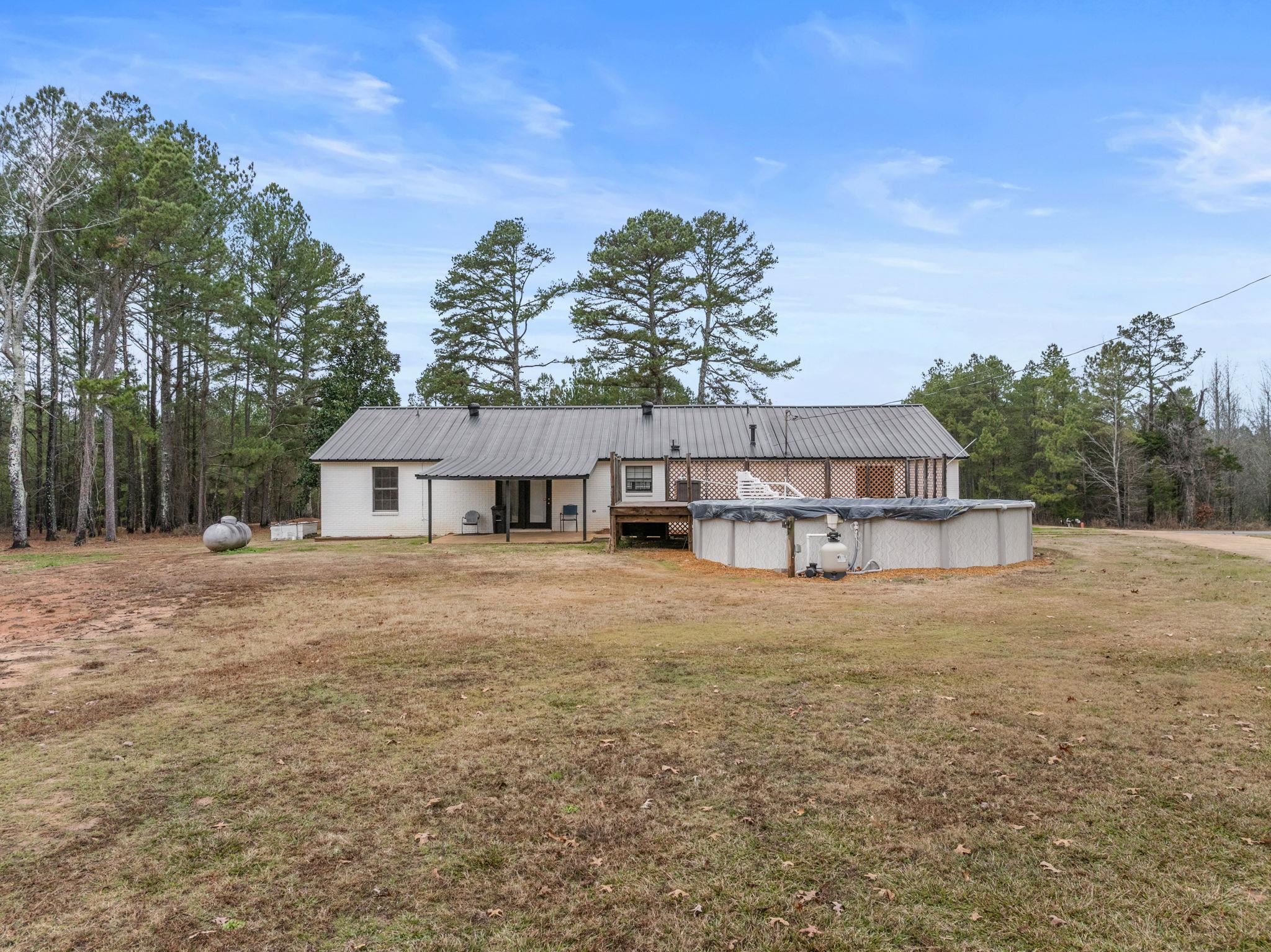 310 County Road 638 Corinth, MS 38834 - Photo 17 of 40 Back of property featuring a covered pool, a lawn, and a metal roof