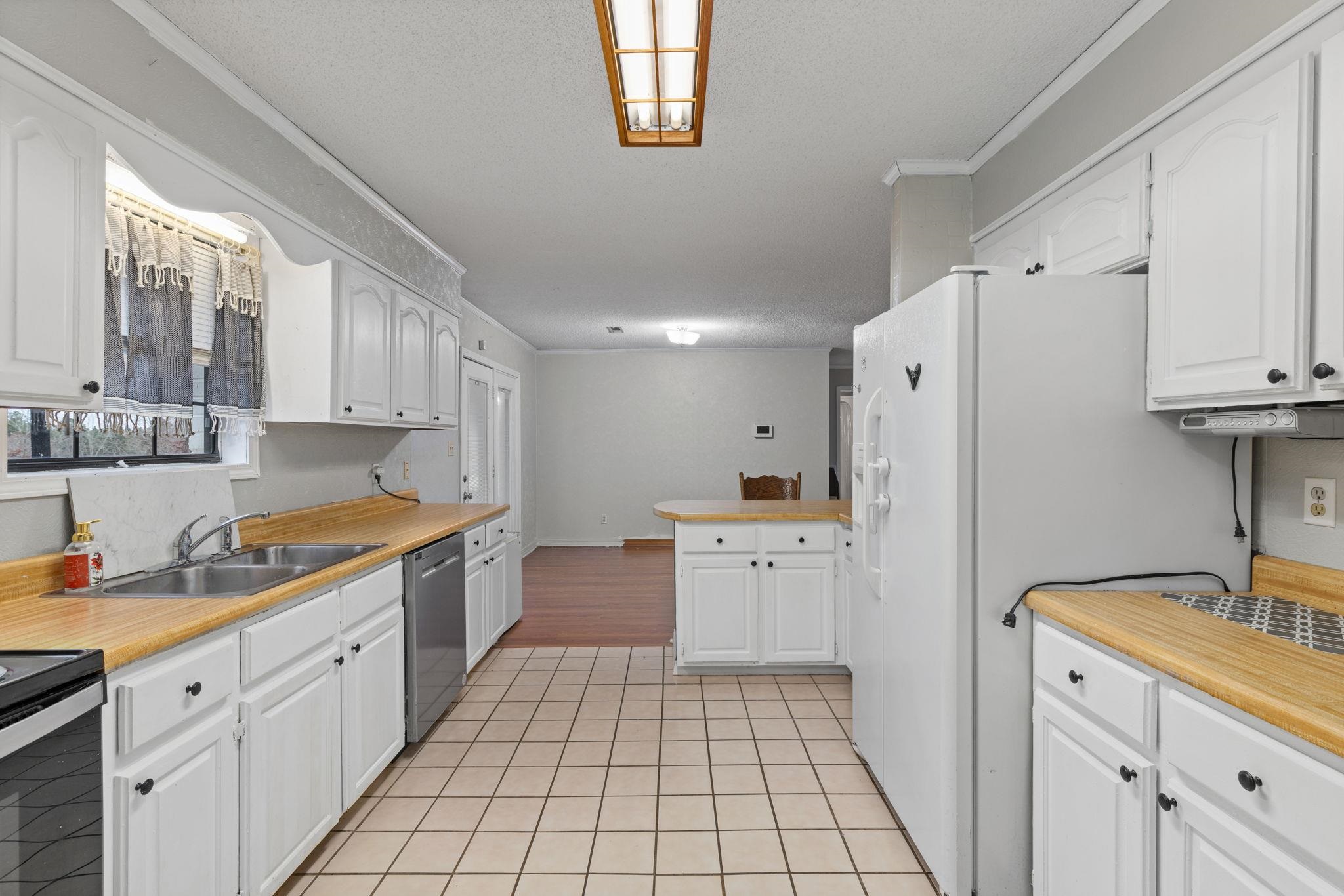 310 County Road 638 Corinth, MS 38834 - Photo 25 of 40 Kitchen featuring light countertops, white refrigerator with ice dispenser, white cabinetry, crown molding, and dishwasher