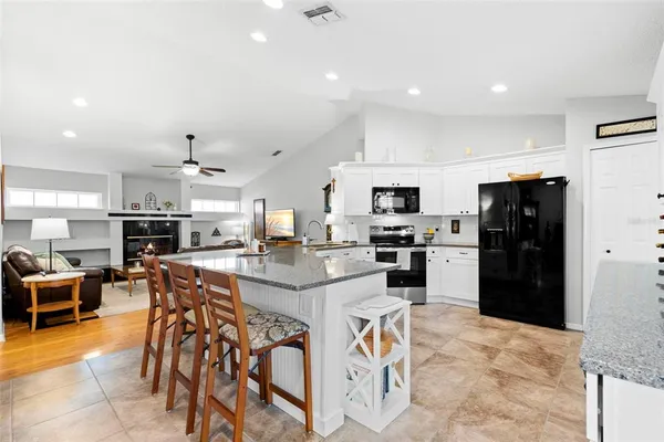 a kitchen with stainless steel appliances kitchen island granite countertop a refrigerator a stove a sink a dining table and chairs with wooden floor