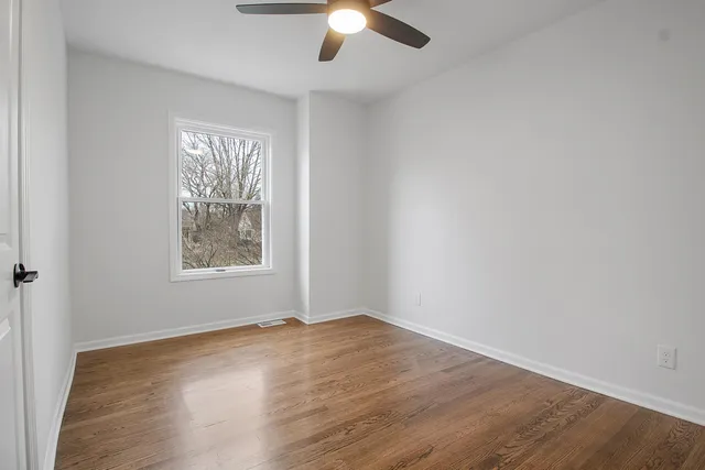 an empty room with wooden floor chandelier fan and windows