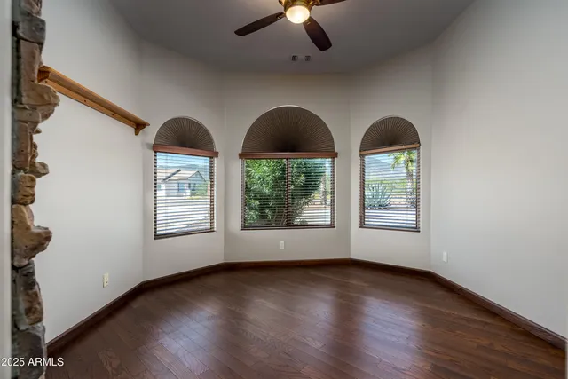 an empty room with wooden floor chandelier fan and windows