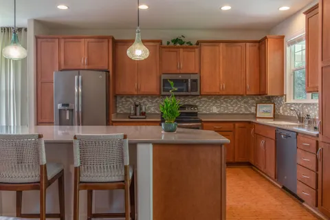 a kitchen with stainless steel appliances granite countertop a refrigerator a sink a stove a dining table and chairs