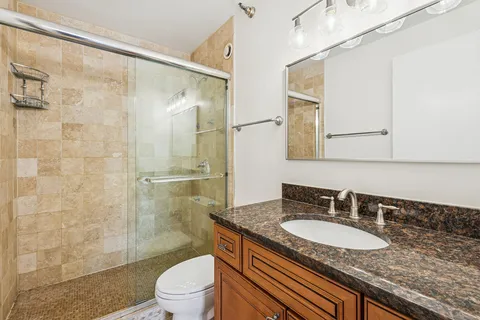 a bathroom with a granite countertop sink a toilet a mirror and shower