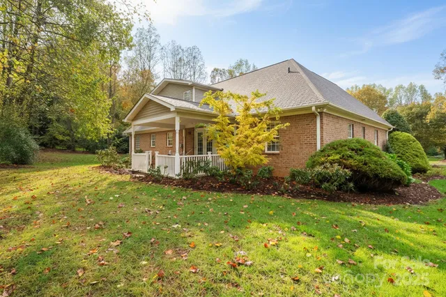 a view of a house with brick walls and a yard with plants and large trees