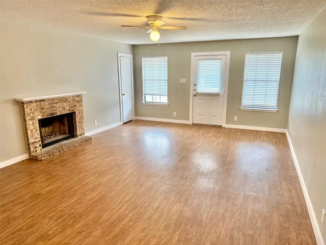 an empty room with wooden floor fireplace and windows