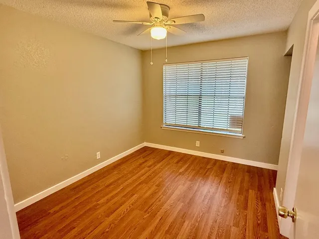an empty room with wooden floor fan and windows