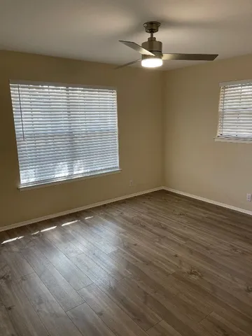 an empty room with wooden floor chandelier fan and windows