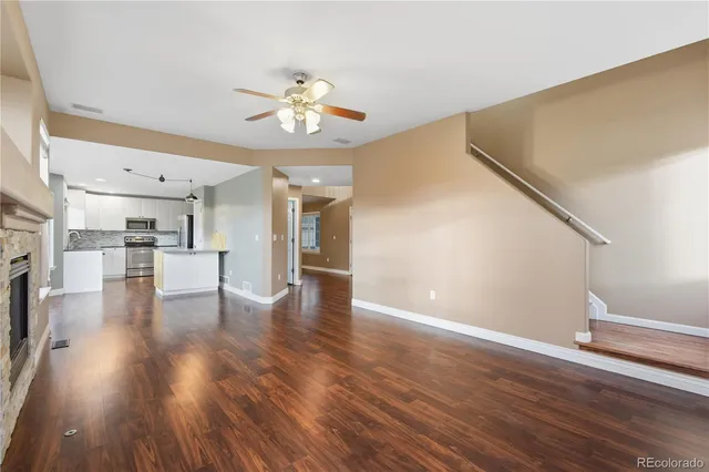 a view of an empty room with wooden floor and a kitchen