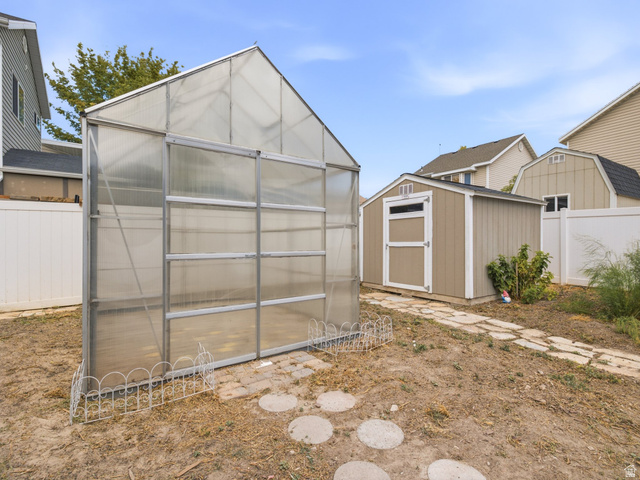 392 West Bricker Road Draper, UT 84020 - Photo 25 of 33 Backyard featuring a greenhouse, a storage shed with a shingle roof, a stepping stone pathway, and vinyl fencing