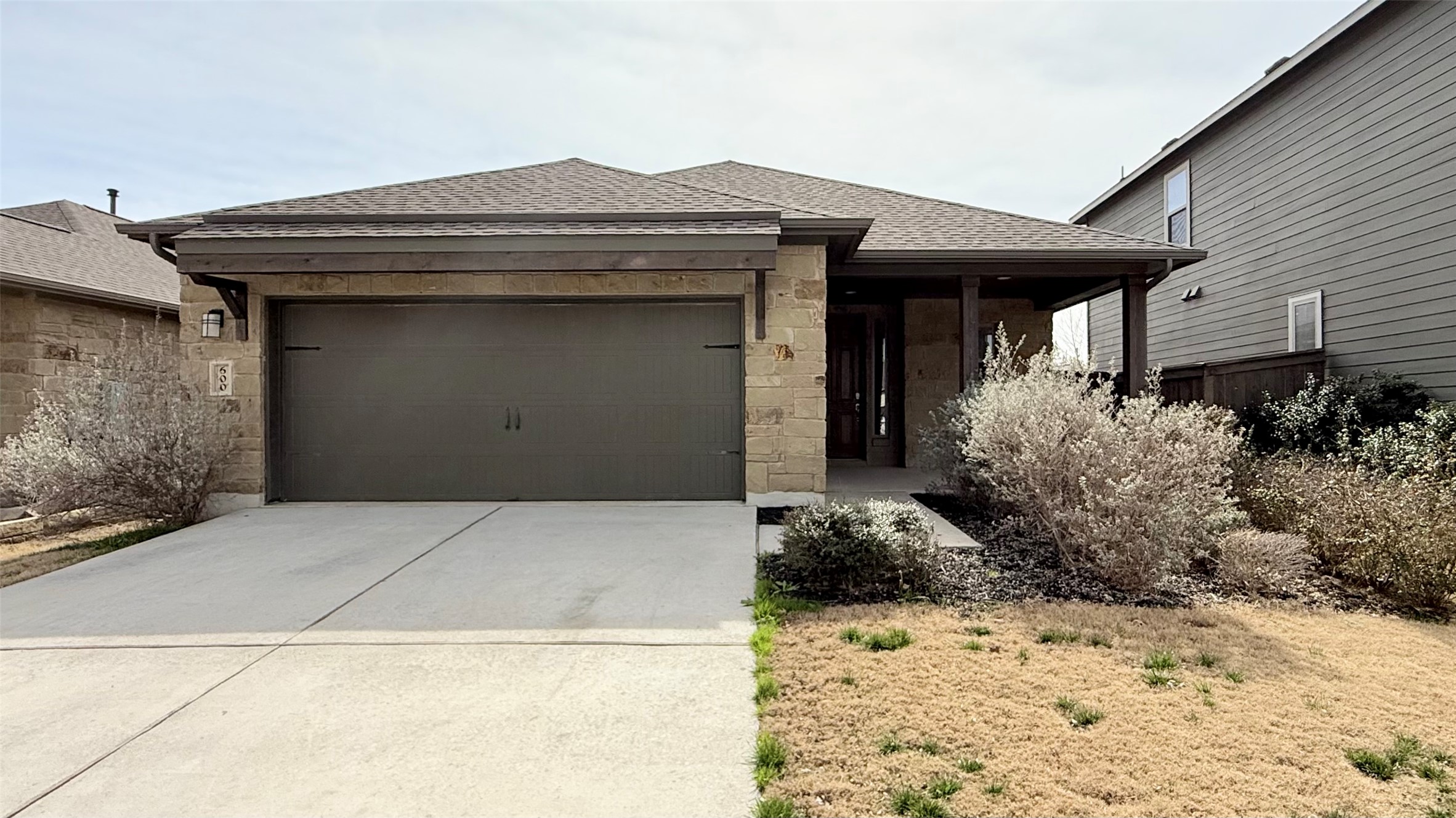 View of front of house with roof with shingles, an attached garage, concrete driveway, stone siding, and covered porch
