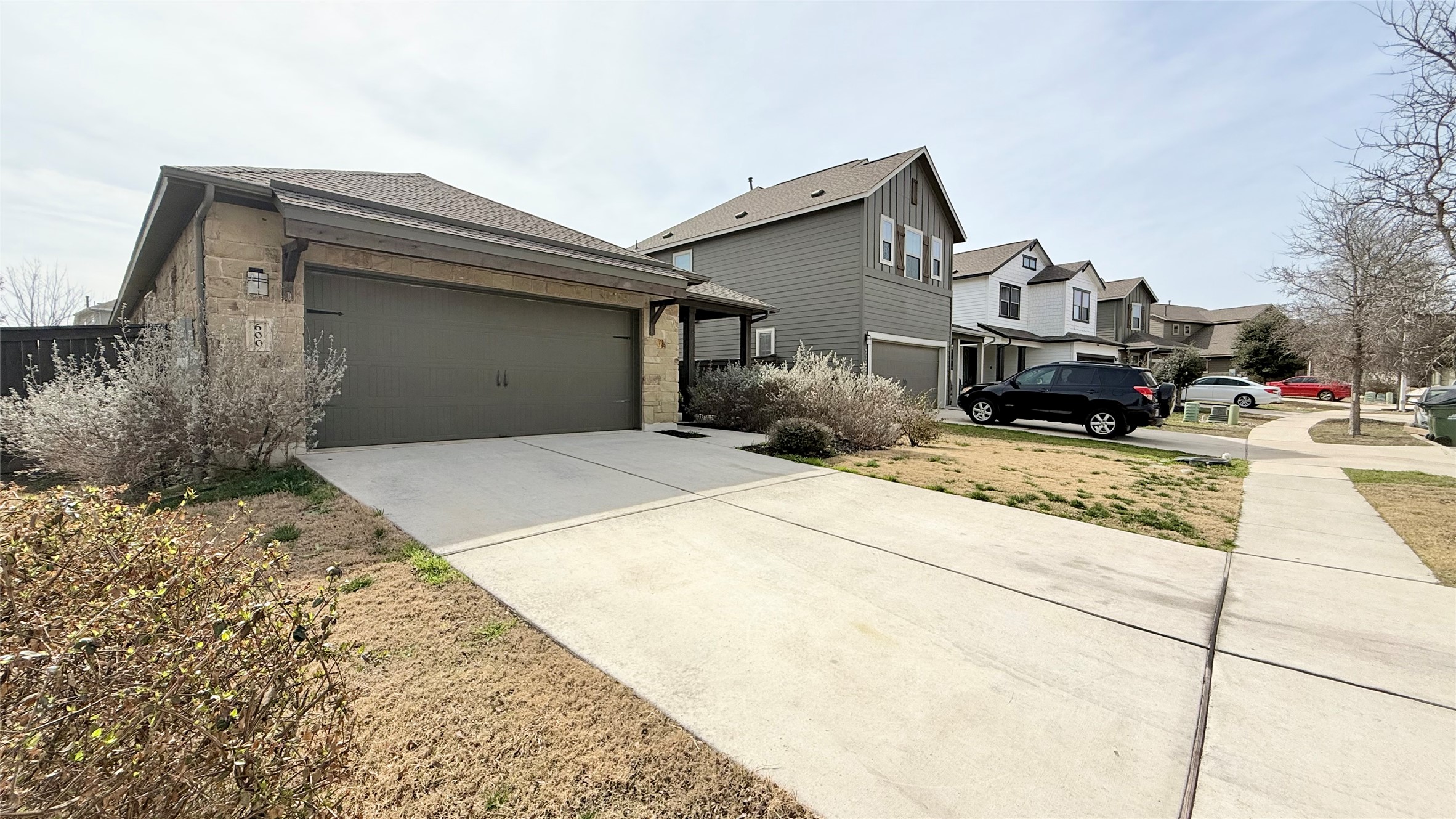 600 Golden Glory Road Leander, TX 78641 - Photo 2 of 21 View of side of home featuring concrete driveway, stone siding, a residential view, a garage, and roof with shingles