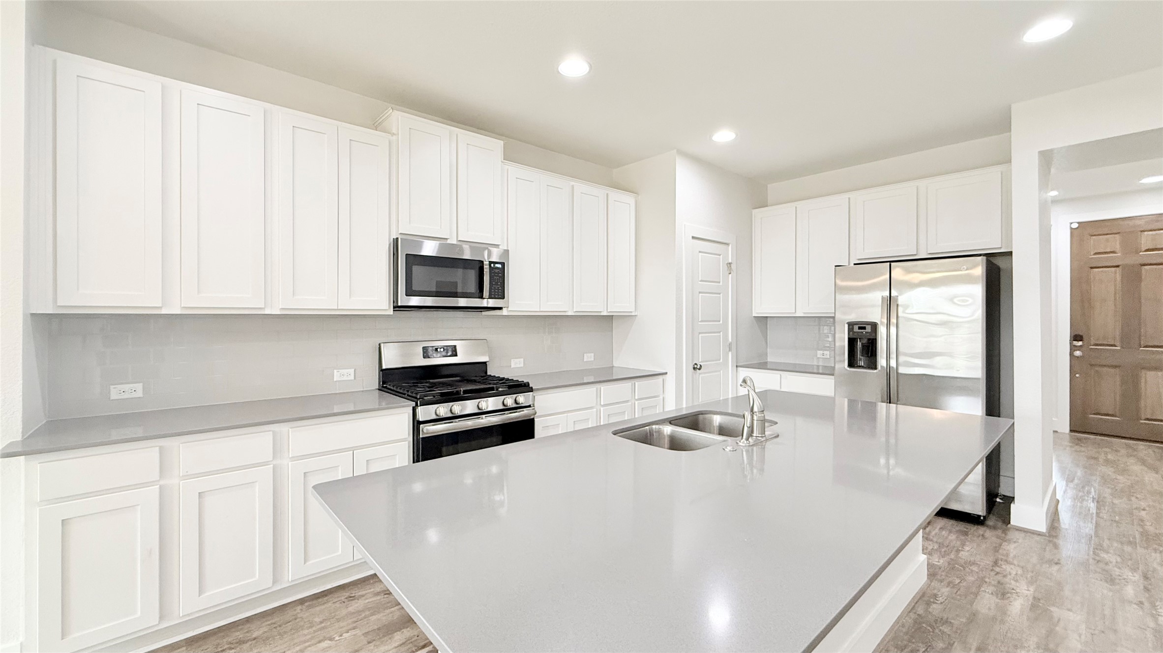 600 Golden Glory Road Leander, TX 78641 - Photo 4 of 21 Kitchen with stainless steel appliances, white cabinets, light wood finished floors, a spacious island, and decorative backsplash