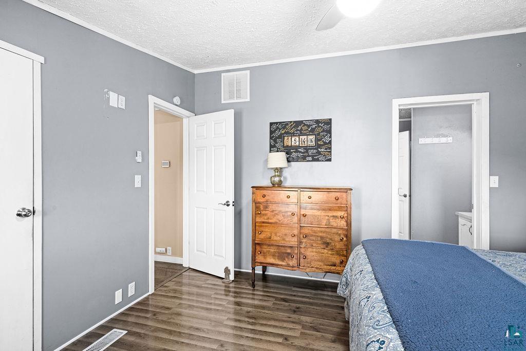 6638 Tabako Road Wright, MN 55798 - Photo 17 of 34 Bedroom with a textured ceiling, crown molding, dark wood-style floors, ceiling fan, and connected bathroom