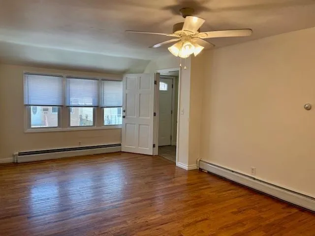 an empty room with wooden floor fan and windows
