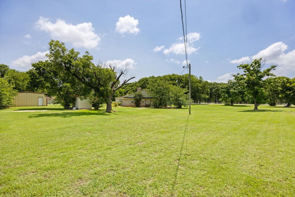 4210 Waples Road Granbury, TX 76049 - Photo 7 of 37 Expansive grassy lot with mature trees, a detached storage building, and a tan metal outbuilding featuring a white service door