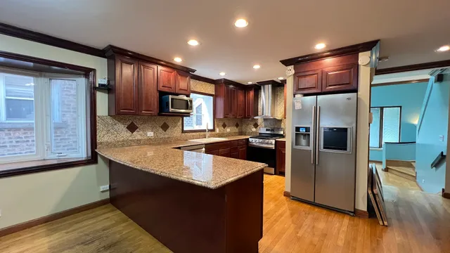 a large kitchen with stainless steel appliances granite countertop a refrigerator a sink and wooden cabinets