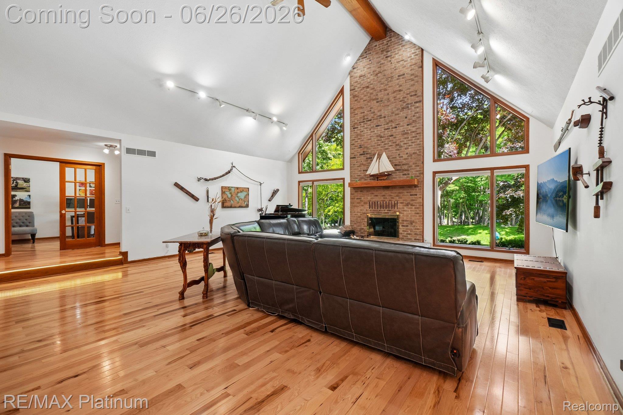 6100 Oak Valley Road Brighton, MI 48116 - Photo 6 of 47 Vaulted ceiling with exposed wood beam, natural wood-finish flooring, and a brick-clad fireplace
