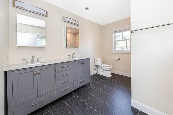 a spacious bathroom with a double vanity sink a mirror and a toilet