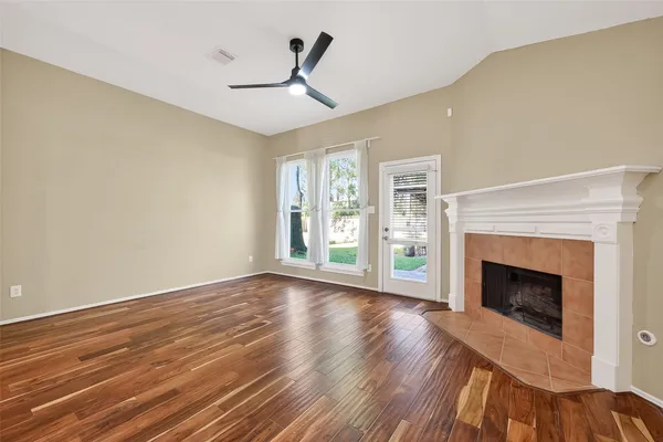 a view of an empty room with wooden floor fireplace and a window