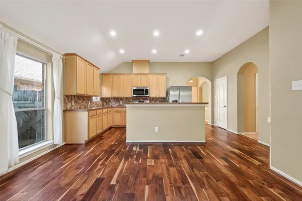 a kitchen with stainless steel appliances granite countertop a refrigerator a sink dishwasher a stove and white countertops with wooden floor