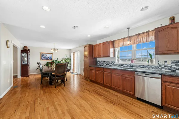 a kitchen with stainless steel appliances granite countertop a stove a sink dishwasher and a dining table with wooden floor