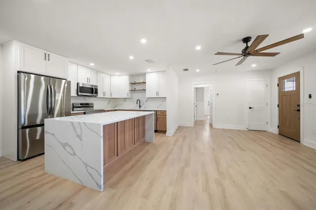 a kitchen with stainless steel appliances a refrigerator a sink dishwasher a oven and a dining table with wooden floor