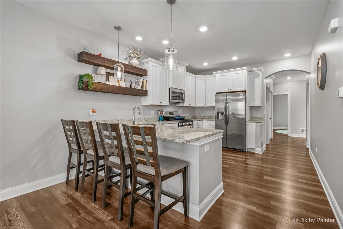 745 Harper Avenue Cary, IL 60013 - Photo 7 of 32 a kitchen with stainless steel appliances granite countertop a kitchen island a stove a refrigerator a oven a sink a dining table and chairs with wooden floor