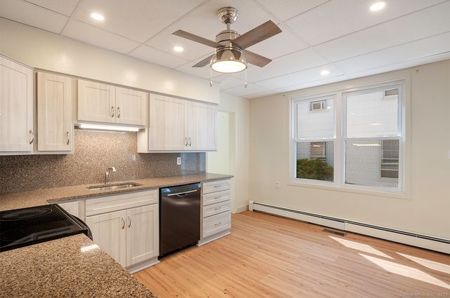 a kitchen with stainless steel appliances granite countertop a sink dishwasher a stove and white cabinets with wooden floor