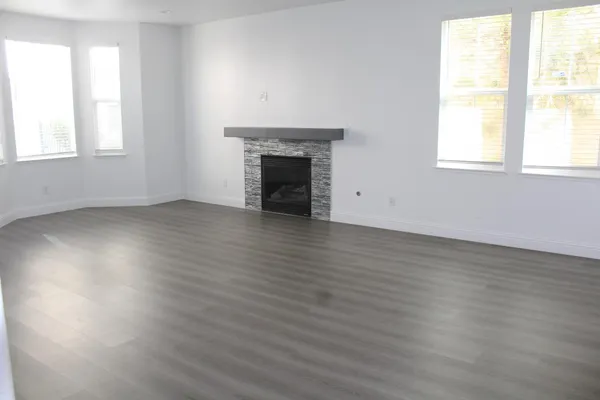 an empty room with wooden floor fireplace and windows