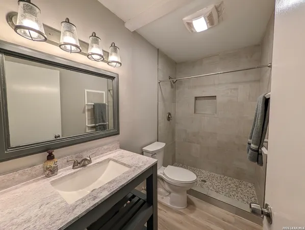 a bathroom with a granite countertop sink a toilet a mirror and shower