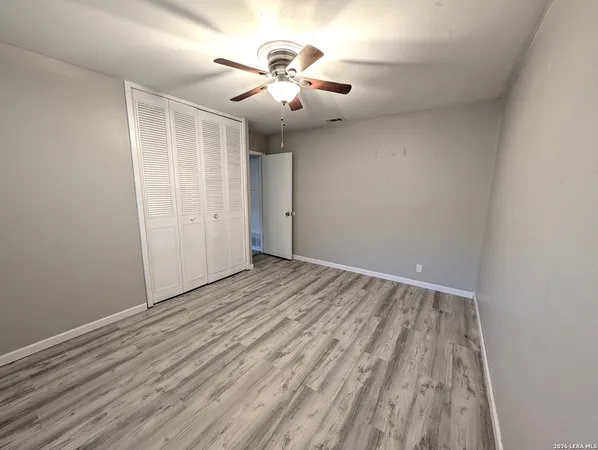 an empty room with chandelier fan and wooden floor