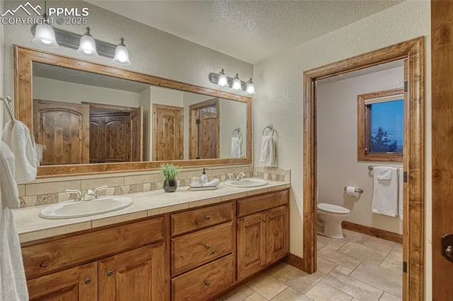 a spacious bathroom with a double vanity sink a large mirror and a toilet