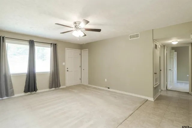 a view of an empty room with window and chandelier fan
