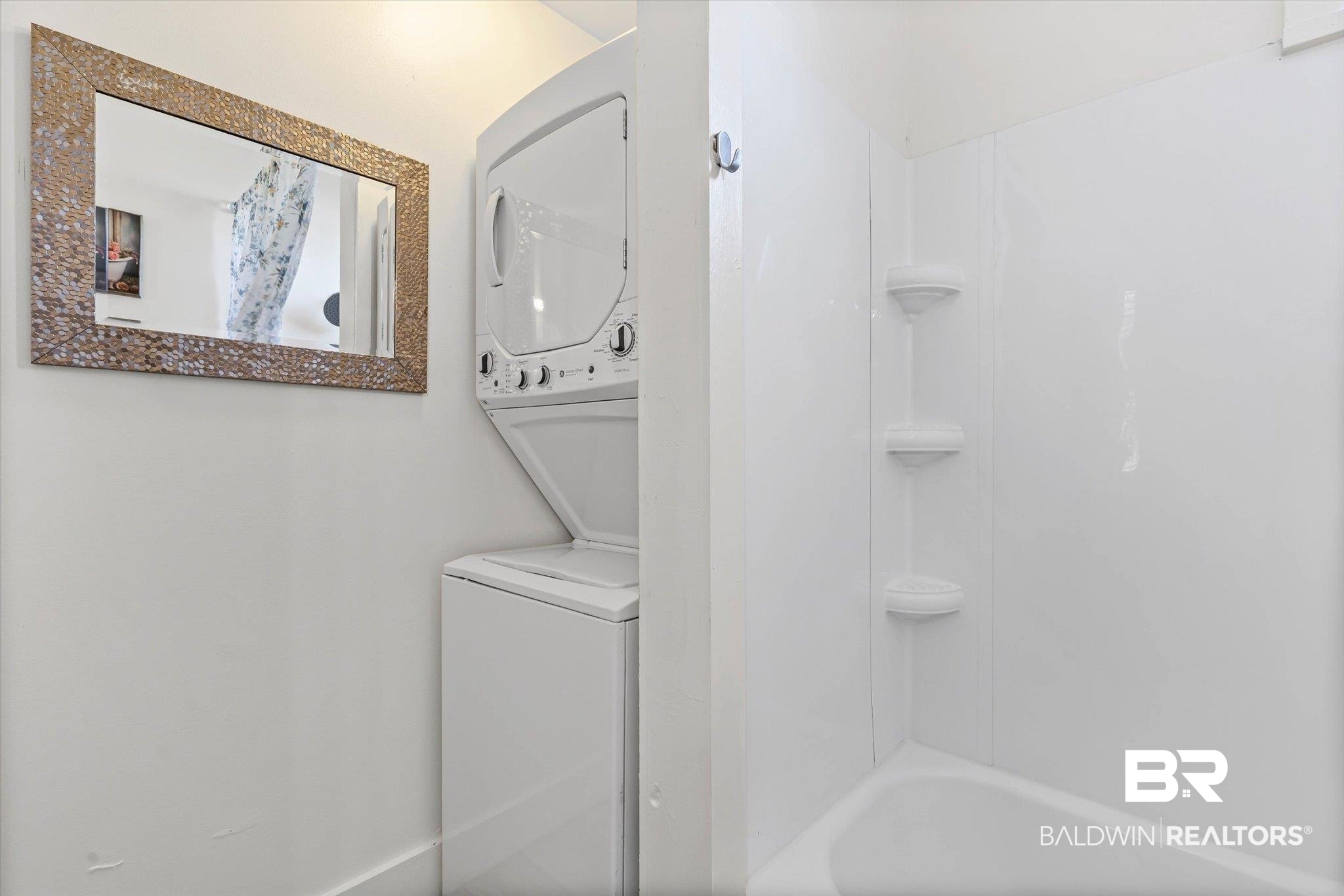 951 Montgomery Street Mobile, AL 36604 - Photo 17 of 22 Compact laundry area featuring a stacked washer and dryer, accompanied by a full bathtub and shower combination with integrated shelving