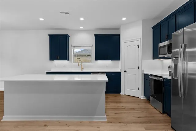 a large kitchen with stainless steel appliances a large counter top a stove and a refrigerator