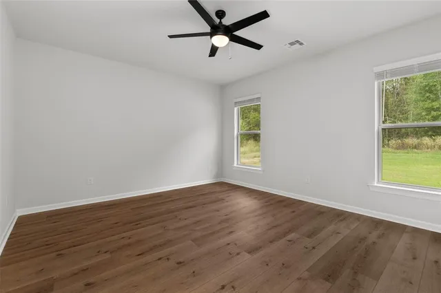 an empty room with wooden floor ceiling fan and windows