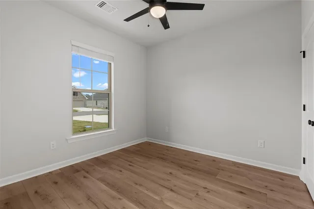 an empty room with wooden floor fan and windows