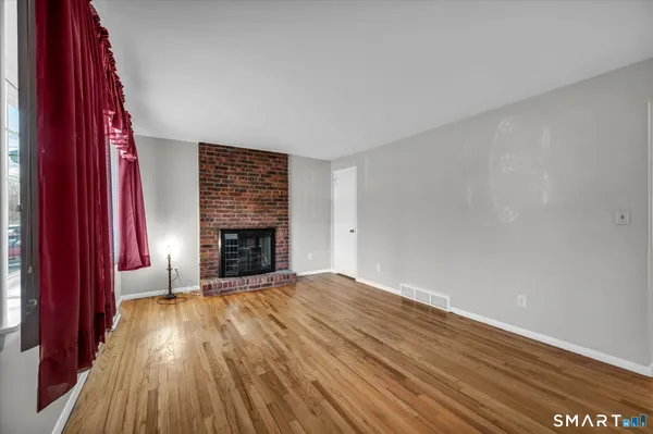 a view of an empty room with wooden floor fireplace and a window