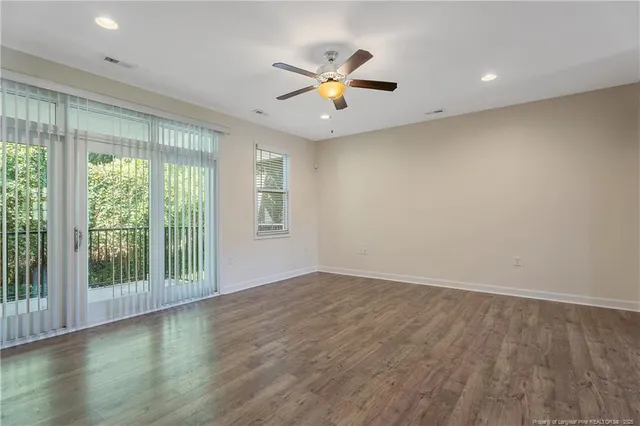 an empty room with wooden floor fan and windows