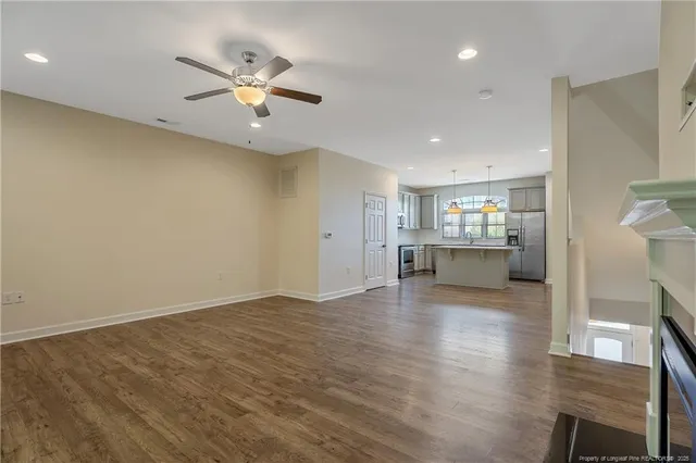 a view of an empty room with kitchen and chandelier fan