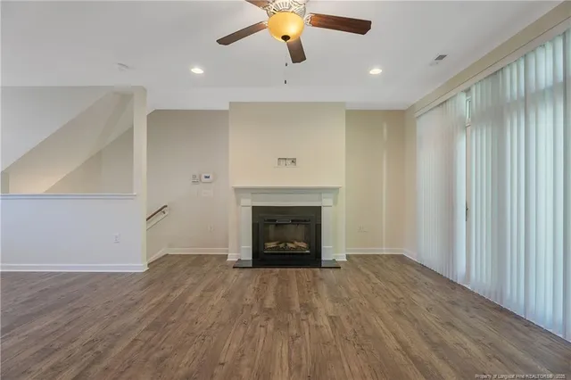 an empty room with ceiling fan fireplace and window