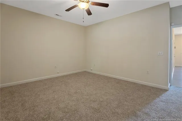 an empty room with a ceiling fan and carpet
