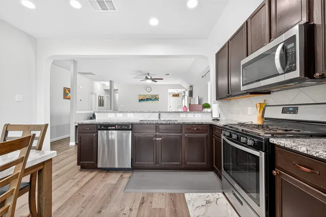 a kitchen with stainless steel appliances granite countertop a stove top oven a sink dishwasher and cabinets with wooden floor