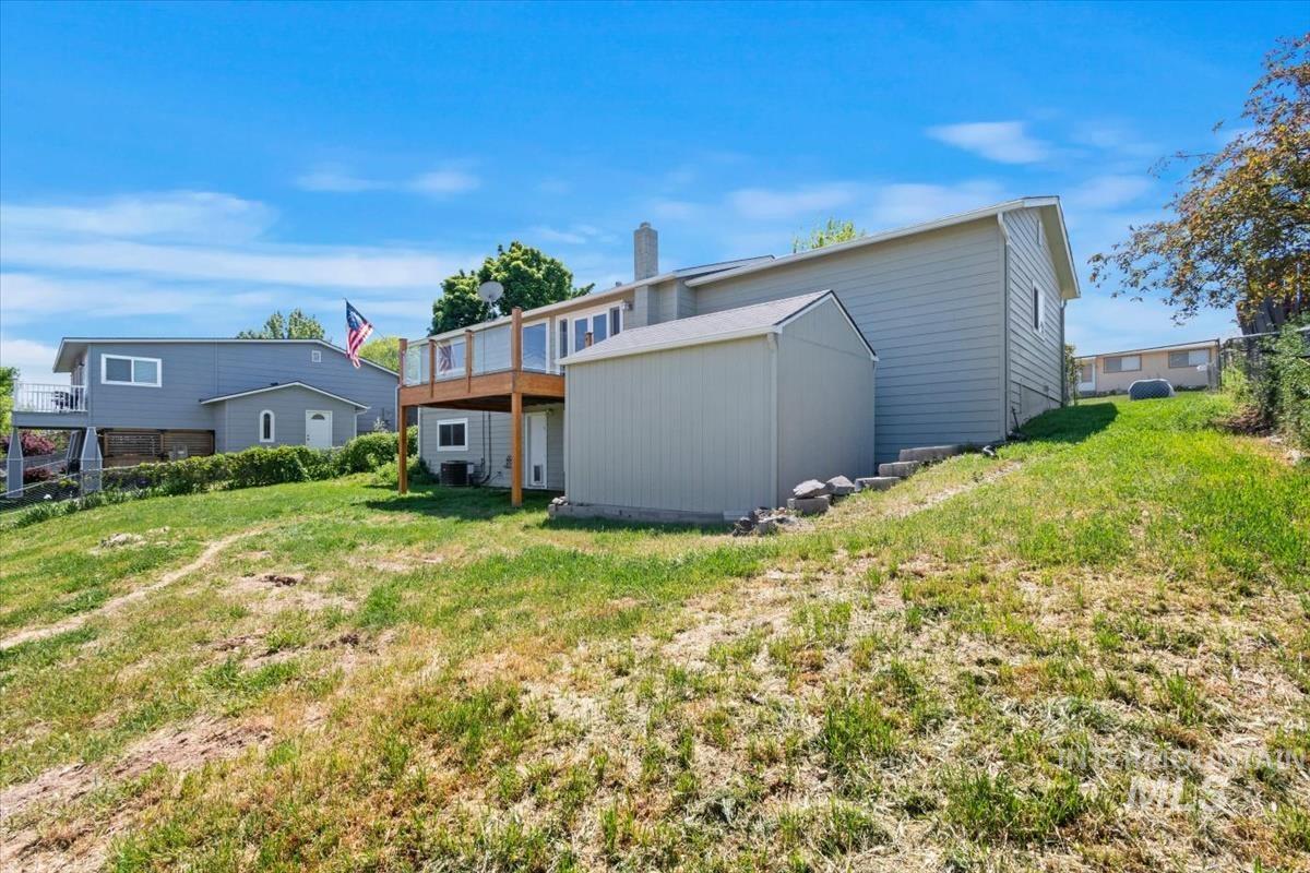 10178 West Fox Ridge Drive Boise, ID 83709 - Photo 30 of 36 Property exterior featuring light gray siding, an elevated wood deck with glass panel railing, and a detached storage shed