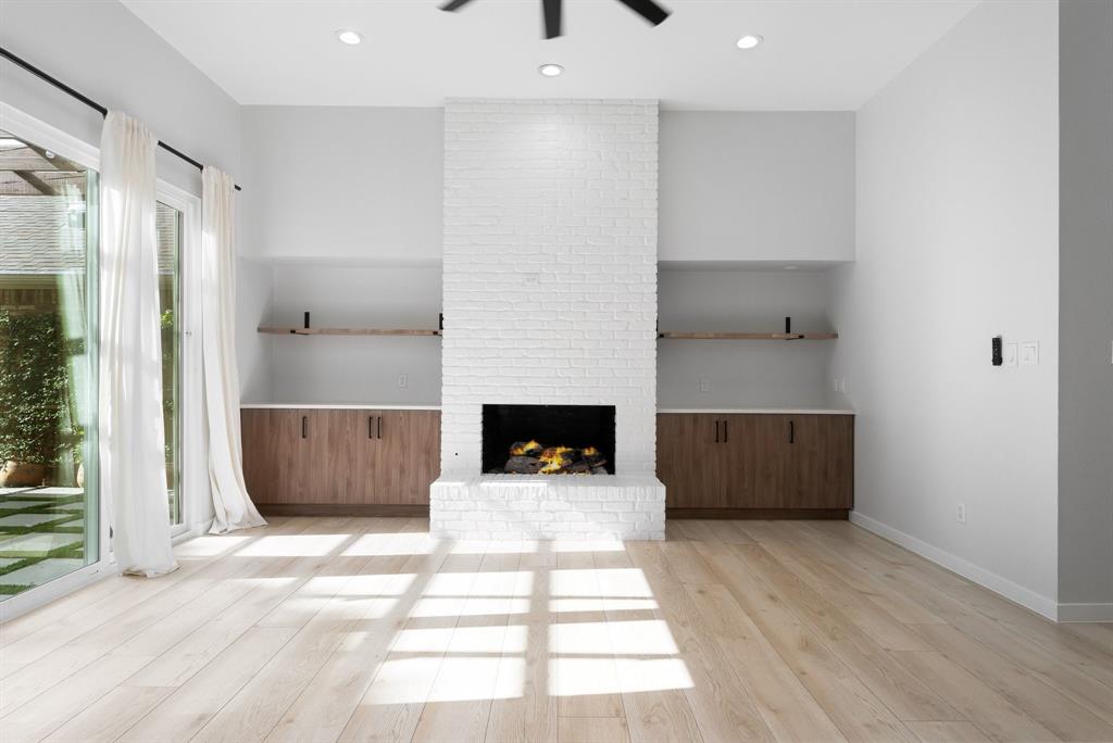 14140 Regency Place Dallas, TX 75254 - Photo 5 of 38 Spacious living area featuring a white brick fireplace, built-in cabinetry with wood-finish doors, open shelving, and light wood-finish flooring