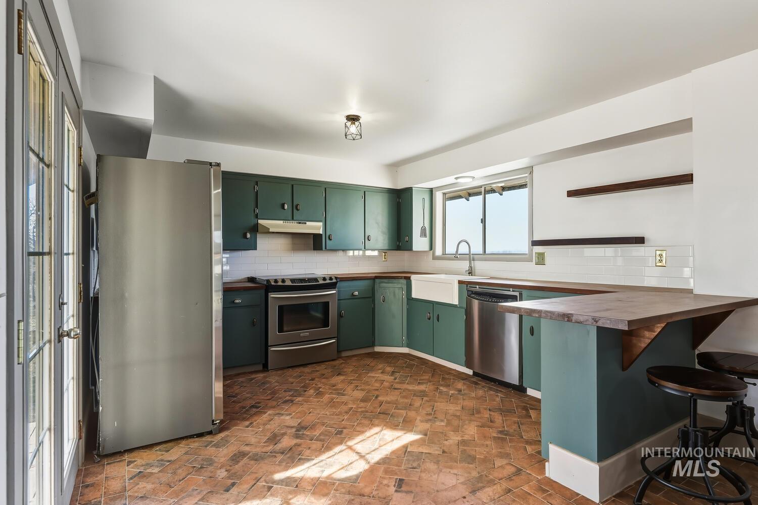22573 Travis Road Wilder, ID 83676 - Photo 12 of 30 Kitchen featuring open shelves, stainless steel appliances, brick flooring, and a kitchen breakfast bar
