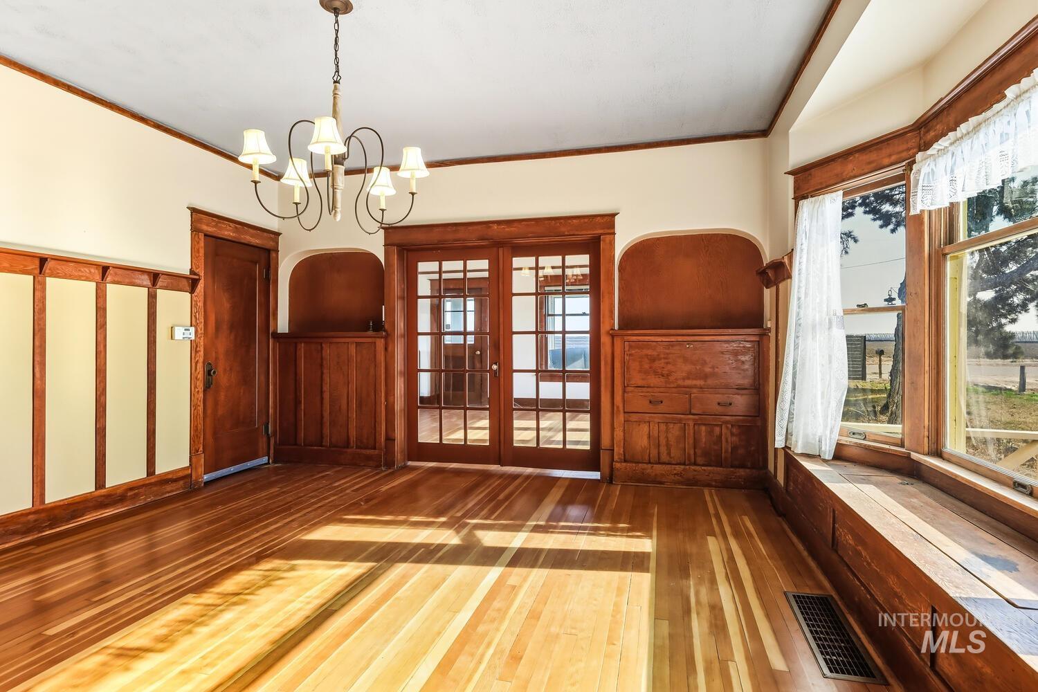 22573 Travis Road Wilder, ID 83676 - Photo 9 of 30 Unfurnished dining area with hardwood / wood-style flooring, french doors, wainscoting, ornamental molding, and a chandelier