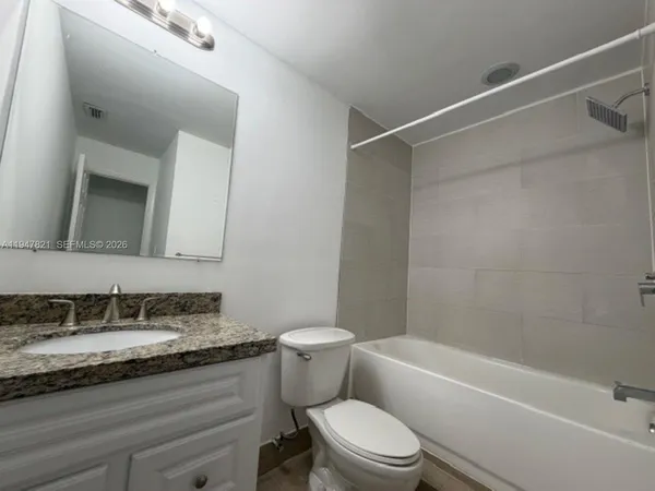 a bathroom with a granite countertop bathtub shower sink vanity mirror and toilet