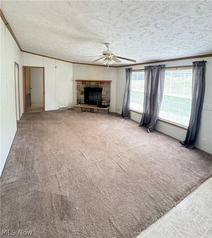 28240 Osborne Road Coolville, OH 45723 - Photo 4 of 29 Unfurnished living room featuring ornamental molding, carpet floors, a ceiling fan, a stone fireplace, and a textured ceiling